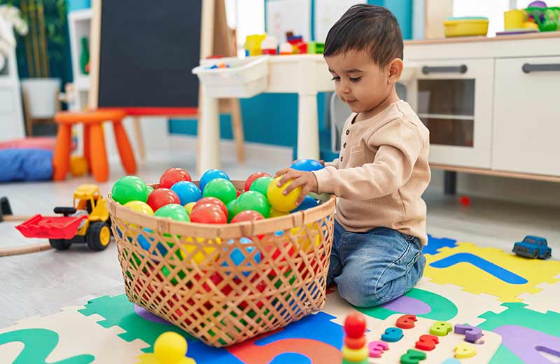 adorable hispanic toddler playing with balls sitting floor kindergarten